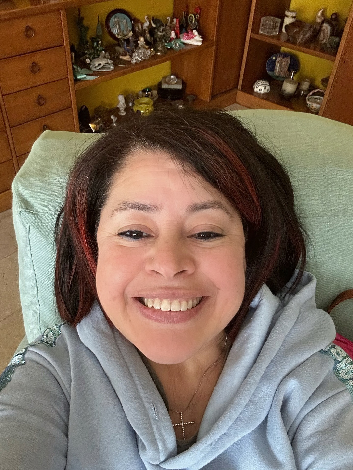 Marisol, sorriso ravvicinato, capelli scuri con riflessi rossi, felpa azzurra. Autoritratto in casa.